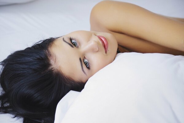 A girl with dark hair is lying on the bed