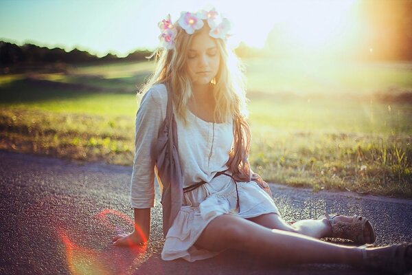 A girl is sitting on the road against the background of the sun