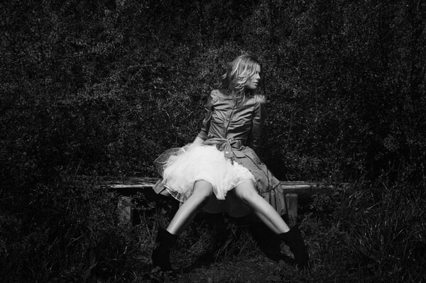 Black and white photo of a girl on a bench in a white dress