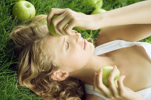 Niña yace en la hierba con manzanas en sus manos