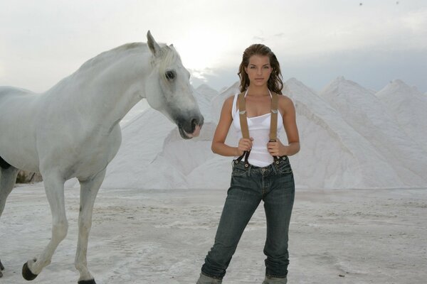 Caballo blanco e Yvonne Catterfeld en la arena contra el fondo de las montañas