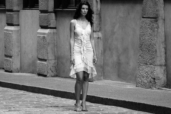 A brunette in a white dress and shoes walks on a tile in the city