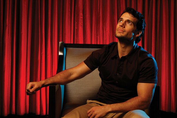 Henry Cavill in a chair against a background of red curtains
