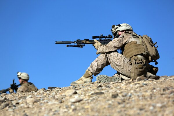 Two soldiers with machine guns in their hands are sitting on the rocks