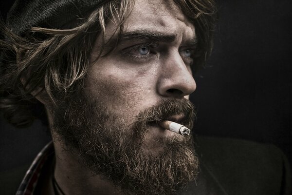 A bearded man in a cap with a cigarette