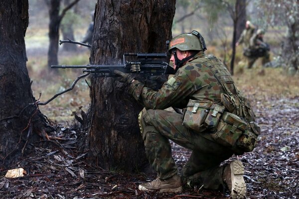 A soldier aims from behind a tree while sitting