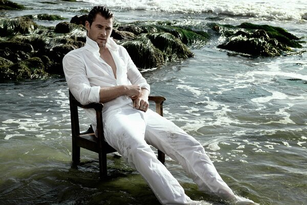Chris Hemsworth attore seduto su una sedia in acqua bagnata in un abito bianco a riposo