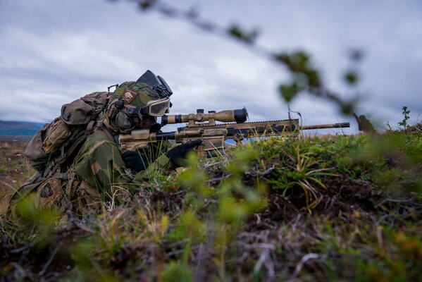 The sniper sitting in the trench keeps his rifle ready