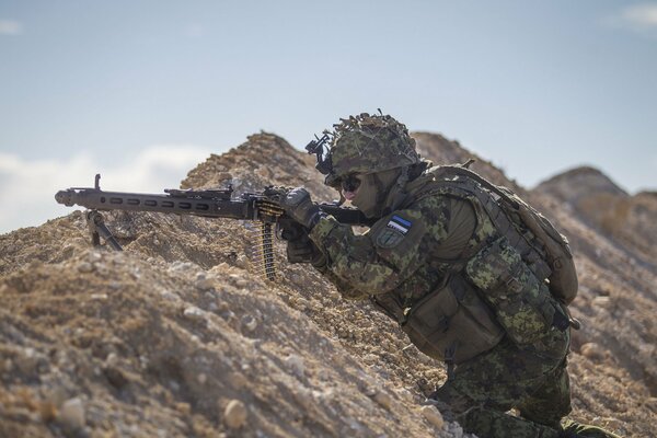 An Estonian soldier with a gun in an ambush on a rock