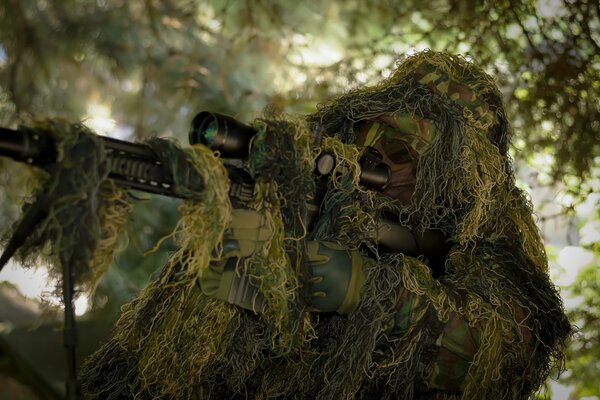 Francotirador con rifle disfrazado en el verde