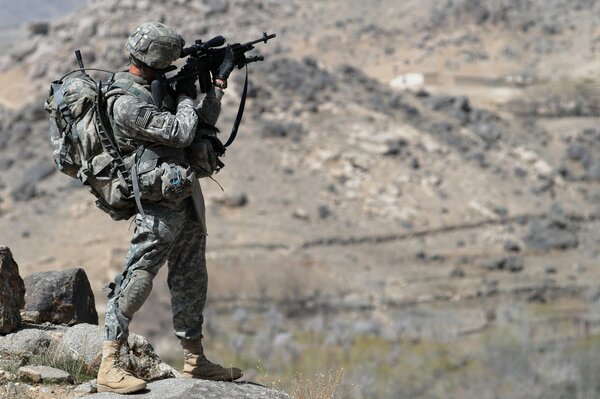 Soldato con armi in piedi su una riva rocciosa