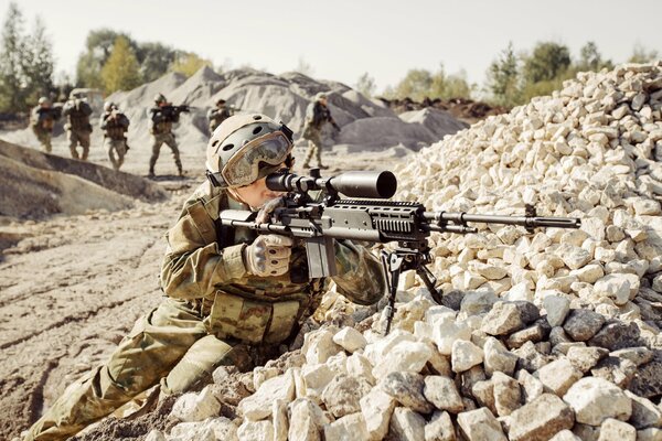 A soldier looking through a telescopic sight lying on the rocks