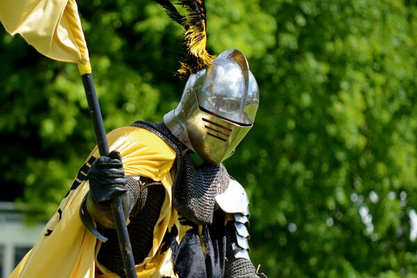 A knight in armor with a yellow cloak and a helmet with feathers