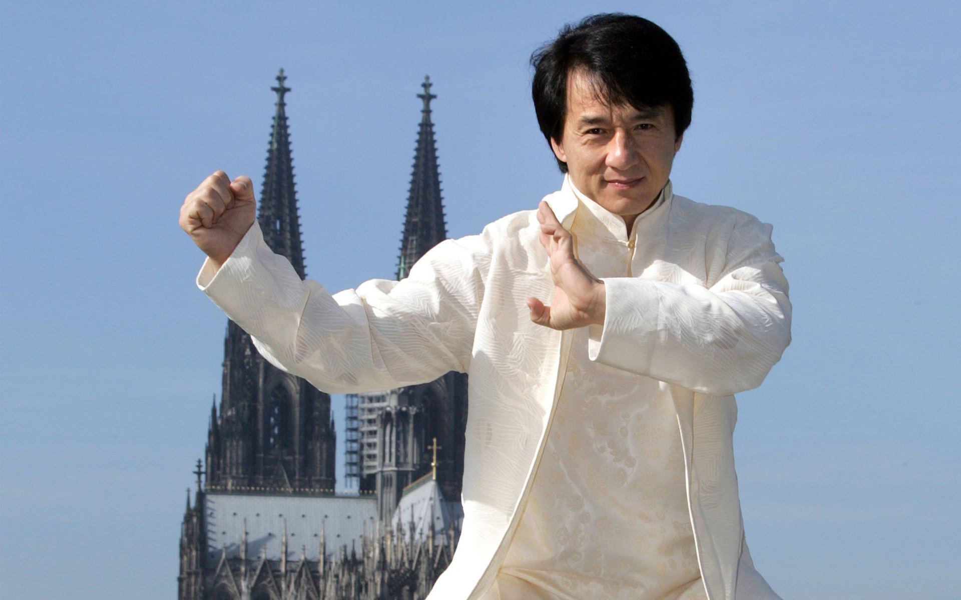 jackie chan acteur réalisateur cascadeur célébrité chinois joie sourire stand poing paume kung fu costume blanc ciel