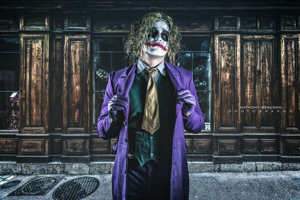 The Joker is standing in a purple raincoat