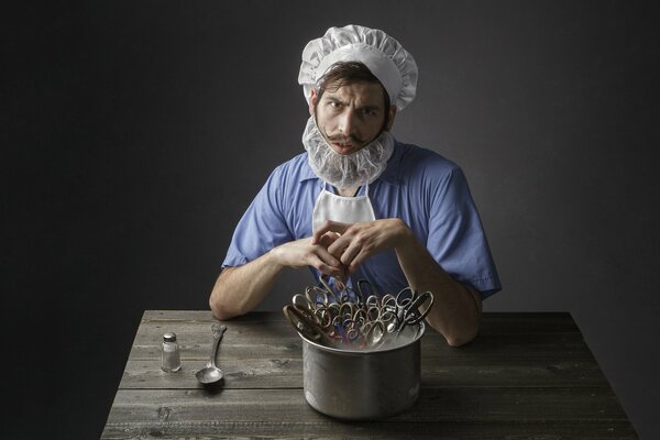 A man in a barber s suit is sitting at a wooden table in front of a pot with scissors