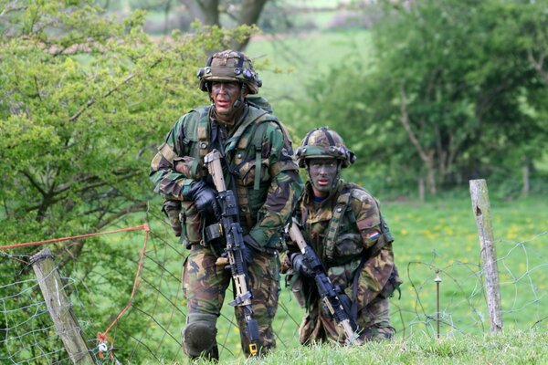 Deux soldats armés se déplacent sur un champ vert parmi les arbres