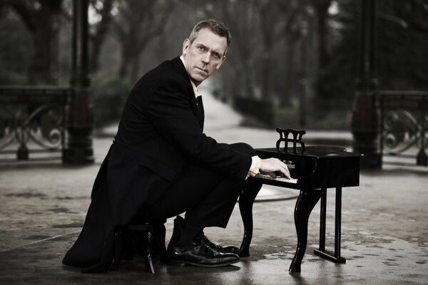 Hugh Laurie in a tailcoat playing the piano in the park