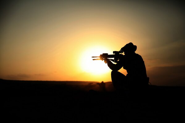 Silhouette of a soldier with a machine gun at sunset