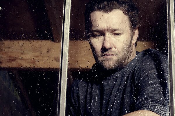 Thoughtful and sad Joel Edgerton at the window with raindrops