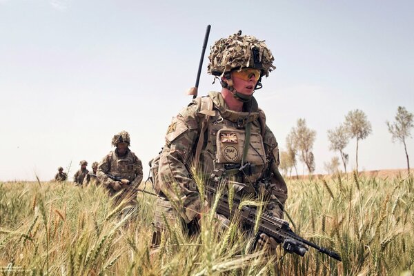 Soldiers in camouflage, with weapons at the ready, walking among the tall grass