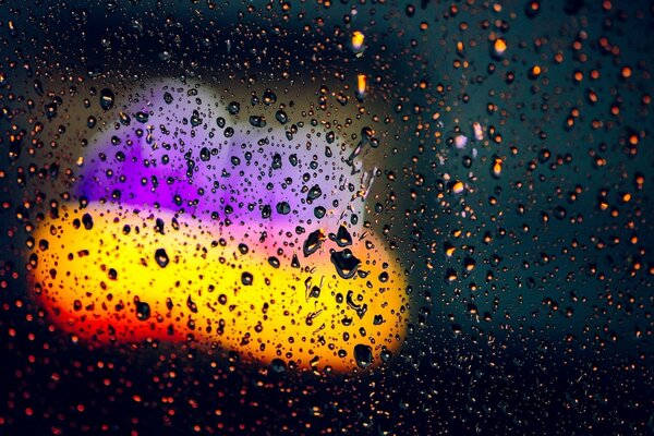 Gouttes de pluie sur le verre avec des lumières jaunes et violettes