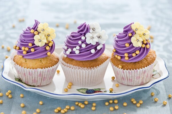 Tres cupcakes en un plato con crema púrpura y flores