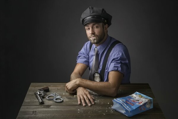 Poliziotto in posa per una foto. Sul tavolo c è un revolver, manette e un sacchetto di ciambelle