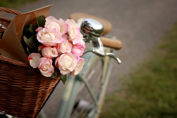 Un ramo de flores rosas se encuentra en una cesta de pie en una bicicleta