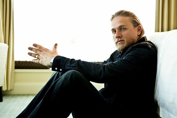 Charlie Hunnam si siede sul pavimento e guarda la telecamera