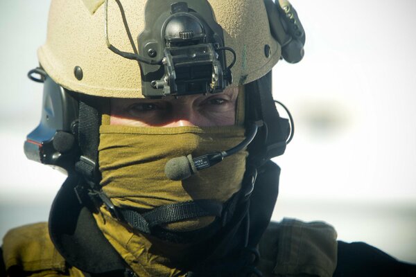 A soldier in equipment stands with a microphone and looks