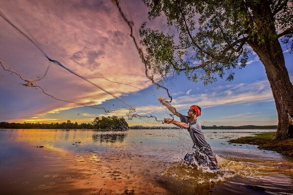 Pêcheur jette un filet sur la rivière au coucher du soleil