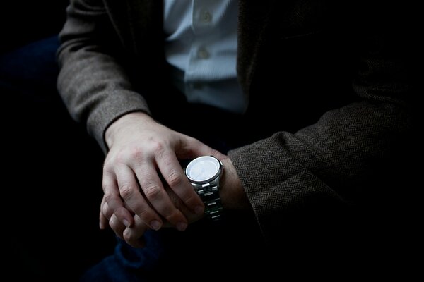 Человек в пиджаке смотрит на наручные часы, определяет время
