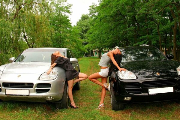 Two girls posing near two cars