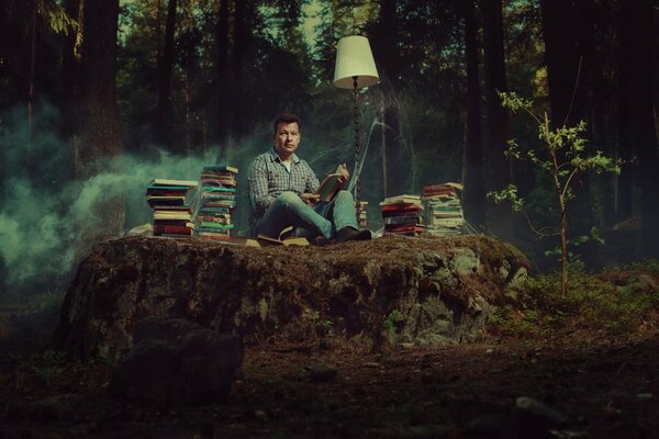 Книголюб сидит посреди леса с книгами и лампой