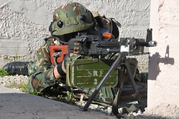 A soldier with a gun aims lying down