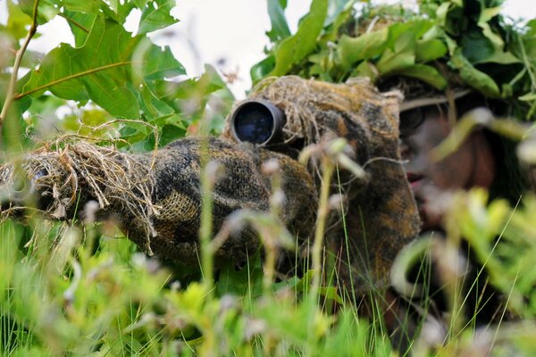 Maskierter Scharfschütze mit Gewehr im Gras