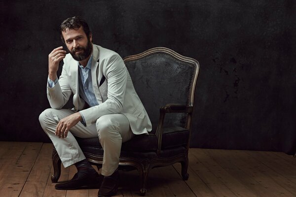 James Piurfoy en un traje blanco sentado en una silla