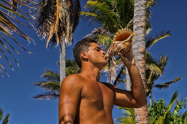 A tanned guy on the background of palm trees holds a sink