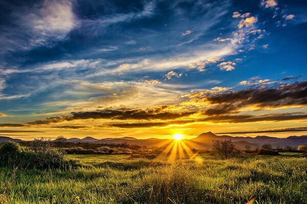 Al atardecer, los rayos del sol envuelven el campo y las montañas