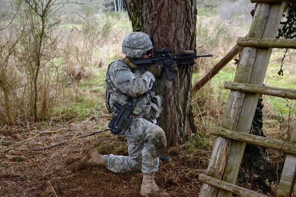 A man with a gun hides behind a tree