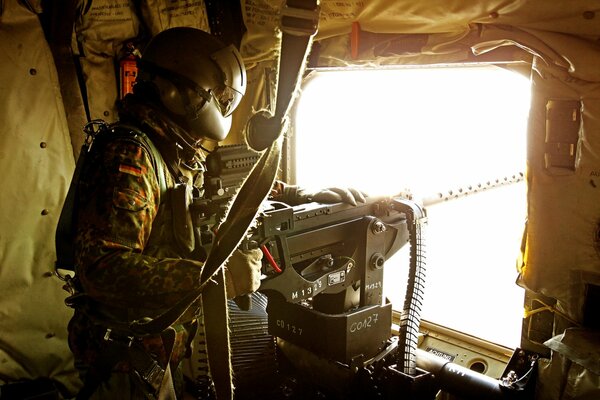 A soldier aims a weapon from a helicopter