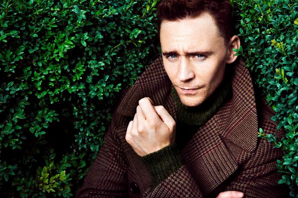 Actor Tom Hiddleston in a coat on a green background