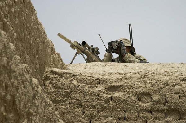 A soldier watches the enemy with a sniper rifle
