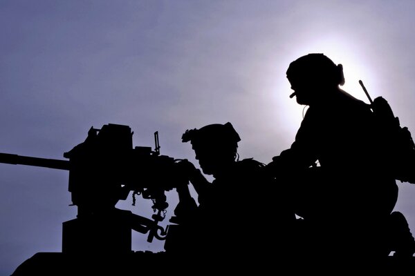 Silhouettes de deux soldats et une mitrailleuse sur fond de ciel