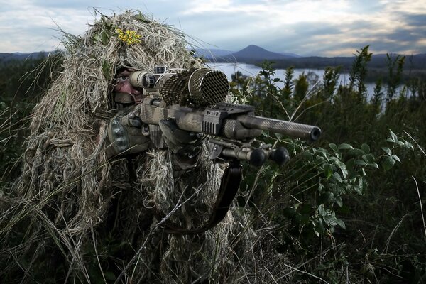 A sniper in the grass takes aim with a weapon