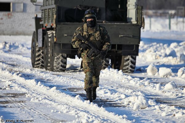 A Russian special forces soldier with a weapon on the background of a truck in winter