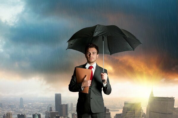 A guy in a suit with a red tie, a beige folder and an open black umbrella stands in the rain against the background of the city and the dawn