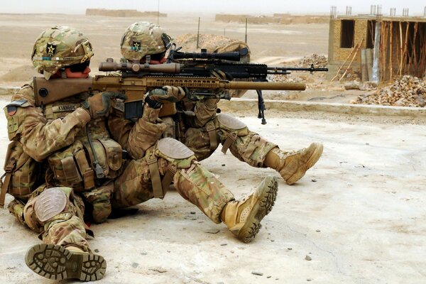 Two soldiers shoot while sitting on the ground