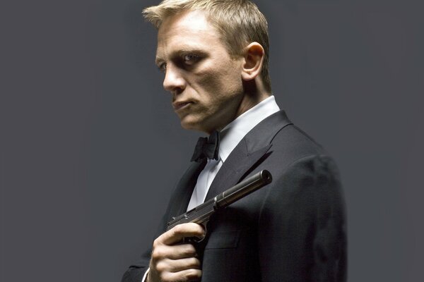 Actor Daniel Craig, who played James Bond, with a gun in his hands on a gray background